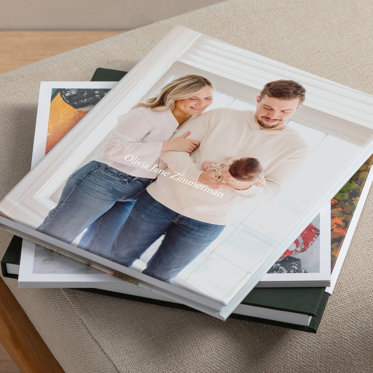 A stack of three photo books from Mpix. The top book has a custom cover featuring a photo of parents with a newborn baby. The middle books is a softcover book, and the bottom book has a linen cover with skinny dust jacket.