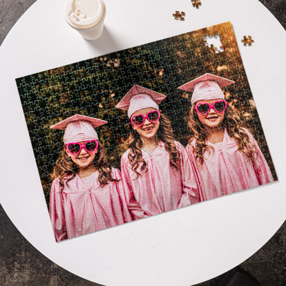 A custom photo puzzle on a table that features an image of three young girls in pink graduating caps and gowns.