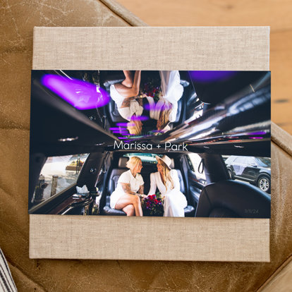 A wedding photo book with a sand color linen cover and skinny dust jacket featuring a photo of two women on their wedding day in a limousine.