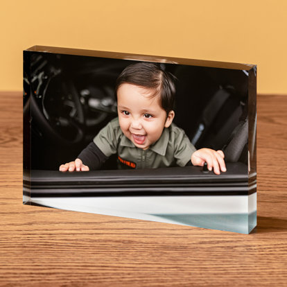 A horizontal acrylic block displayed on a table featuring a photo of a toddler boy standing on the driver seat of a car.