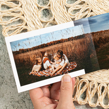 A hand holding an open softcover photo book from mpix on a table placemat with the interior pages showing a photo of a family in a field.