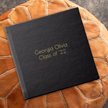 Signature Photo Album from Mpix resting on an ottoman with black leather cover and gold debossing saying Georgia Olivia Class of '22