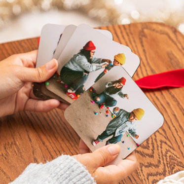 Hands holding a set of four photo coasters from Mpix featuring holiday-themed images of a family.