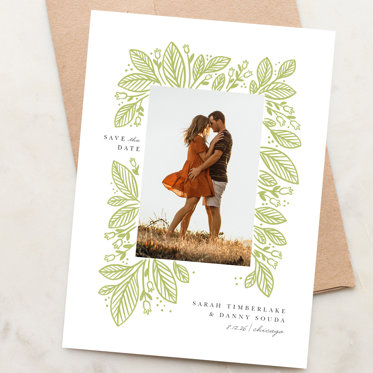 Save the Date card from Mpix resting on a white envelope with a rectangular photo surrounded by flowers and personalized wedding details.