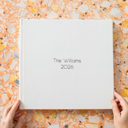 A closed signature photo album with a white leather cover and 'The Williams, 2026' in black foil debossing on the front cover.