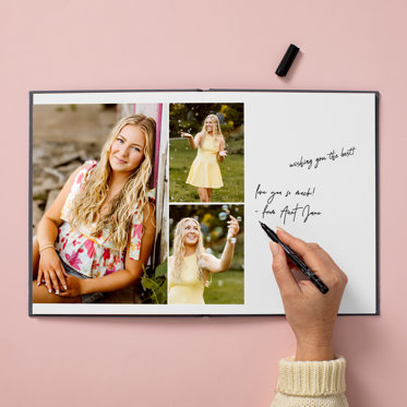 Someone writing a note on the page of an open graduation photo book featuring photos of graduate.