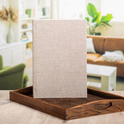 A closed 8.5x11 photo book with a sand color linen cover standing upright on a table. 