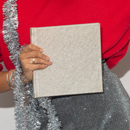 Hands holding a closed 10x10 photo album with a metallic silver leather cover. 