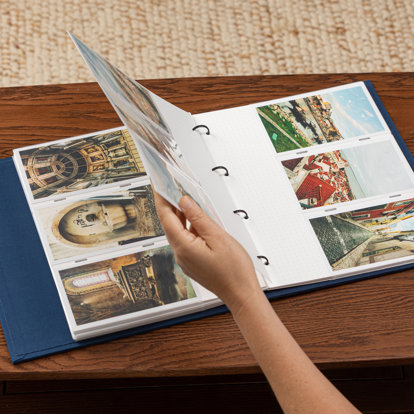 A hand flipping the page of a slip-in photo album showing the pocketed pages that contain photos from a European vacation. 