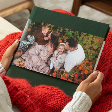 A personalized hardcover photo book with a green linen cover and skinny dust jacket with a personalized photo of a family.