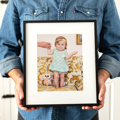man holding a framed print with a white mat, glass, and a thin black frame of a young girl on a couch. 