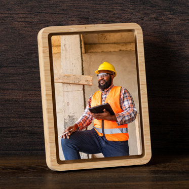 A tabletop framed metal print featuring a photo a construction worker with a hardhat on and holding a tablet.