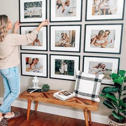 A woman straightening a gallery wall of black-framed family photos