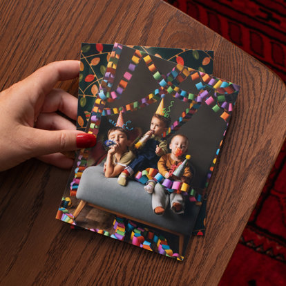 A hand holding a stack of photo prints featuring images of children in party hats at a birthday celebration.