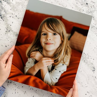 Hands holding a large color photo print featuring a young girl lying on a pillow smiling. 