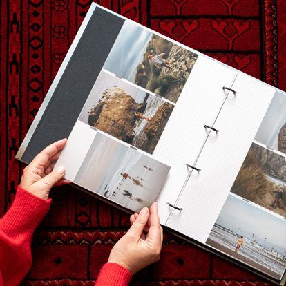 Hands slipping a 4x6 photo of a boy playing on the beach into a pocket of an open slip-in photo album.