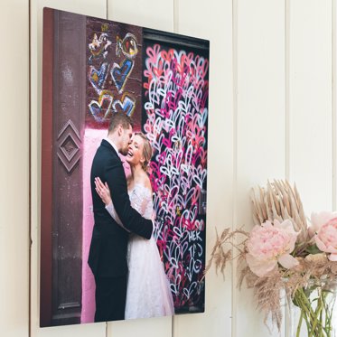 A Metal Photo Print from Mpix mounted on a wooden wall featuring a couple dancing on their wedding day in front of a wall of colorful red, pink, and blue flowers. 