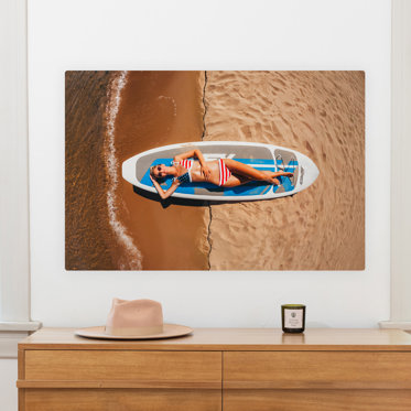 Metal print from Mpix displayed on a wall above a dresser featuring a senior photo of a girl laying on a surfboard on the beach.