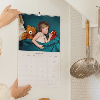 a calendar being hung on a wall using the provided hanger with a photo of a young girl asleep next to her stuffed animals above the calendar grid