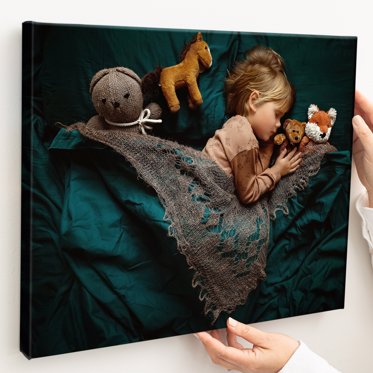 A personalized canvas print wrap from Mpix on a girl asleep next to her stuffed animals with a rich, green velvet blanket. 