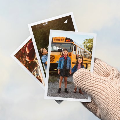 A hand wearing a winter glove holding a stack of photo prints with white borders on the edges.