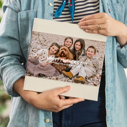 A close up of a person holding a photo book with a tan linen cover and photo dust jacket featuring an image of four young siblings and their pet dog.