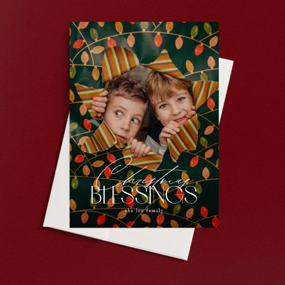 A Christmas photo card featuring two boys peaking out from behind a hole in a wrapping paper covered wall with the text 'Christmas Blessings'.