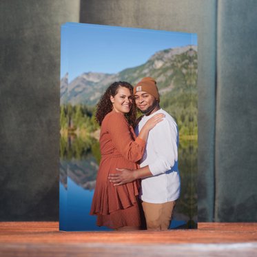 An Acrylic Photo Block from Mpix standing on a desk with a photo of a couple in the mountains by a lake. 