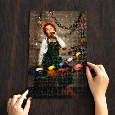 Hands holding an assembled photo puzzle on a table featuring a photo of a child with holiday party decorations.