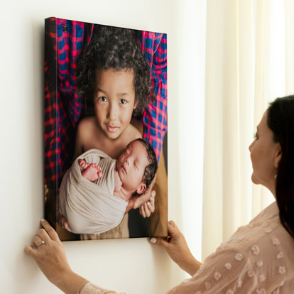 A woman hanging a canvas photo print of her children on the wall