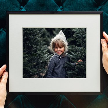 Personalized framed print from Mpix of a toddler in a field of christmas trees with a white mat and thin black metal frame. 