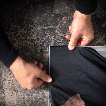 A close up image of hands inserting the sewn edge of a textile print into the assembled frame.