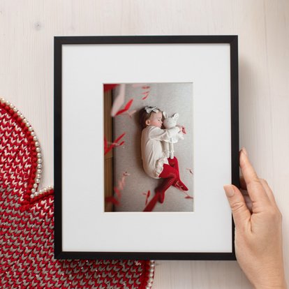 A hand holding a matted and framed print of an image of a young girl sleeping.