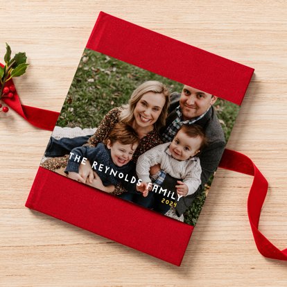 A closed photo book with a red linen cover and skinny dust jacket featuring a family photo and personalized text.