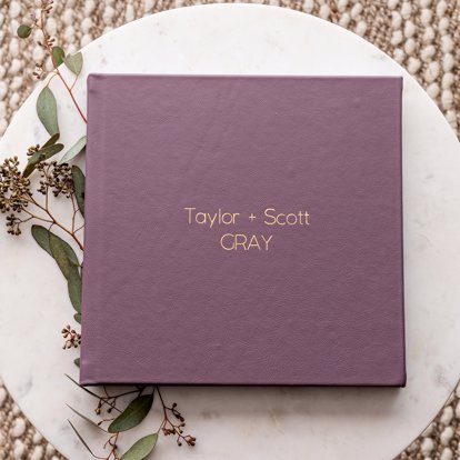 A signature photo album from Mpix resting on a circular table with a purple leather cover and gold debossing saying "taylor + scott gray". 