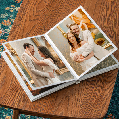 A signature photo album with sand linen cover open to pages featuring photos of a bride and groom holding hands.