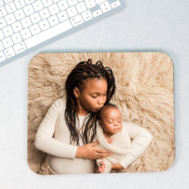 A custom mouse pad from Mpix sitting on a desk featuring a newborn photo with a baby and older sibling.