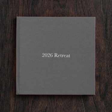 A closed photo book with a charcoal linen cover and the title '2026 Retreat'. 