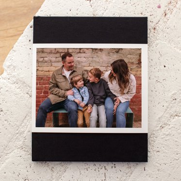 A premium hardcover photo book from Mpix on a table with a pink linen cover and a skinny dust jacket with a colorful photo of a young woman.