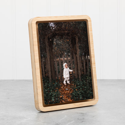 A portrait orientation metal photo print with a floating bamboo wood frame on a table.