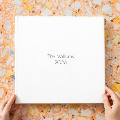 A closed signature photo album with a white leather cover and 'The Williams, 2026' in black foil debossing on the front cover.