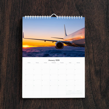 A business photo calendar open to the month of January featuring a picture of airplane above the clouds. 