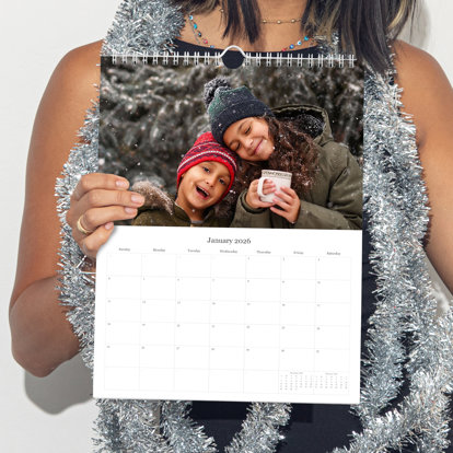 A close up of a person holding a photo wall calendar with a photo on the top half and a calendar grid on the bottom half.