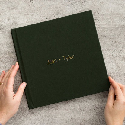 A wedding photo book with evergreen linen cover and the title "Jess + Tyler" in gold debossing on the front cover.