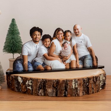 A photo statuette cut out from Mpix of a family of six placed on a wood block on a table with a small christmas tree in the background.