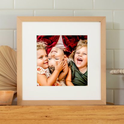 a framed photo print of three young silbings at play with a white window mat and rustic wood frame. 
