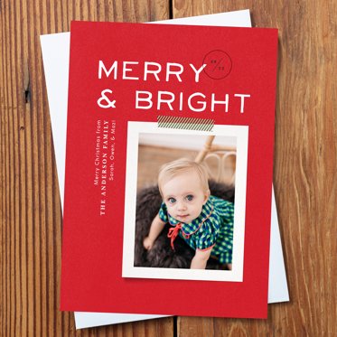 Holiday photo card from Mpix featuring your photo with a thin white frame on a red background with Merry and Bright written in thin white lettering, resting on a white envelope.