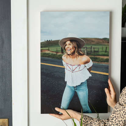 A custom wood print of a woman posing in front of the mountains being hung out on a wall.