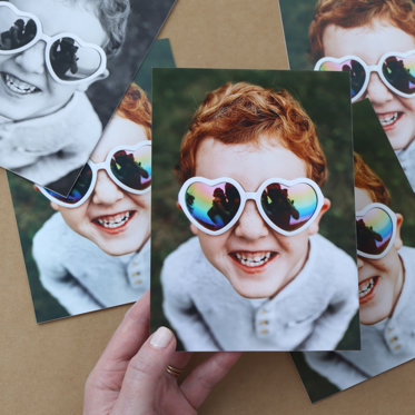 Photo print featuring an up-close shot of a boy wearing heart shaped sunglasses smiling and looking up at the camera.