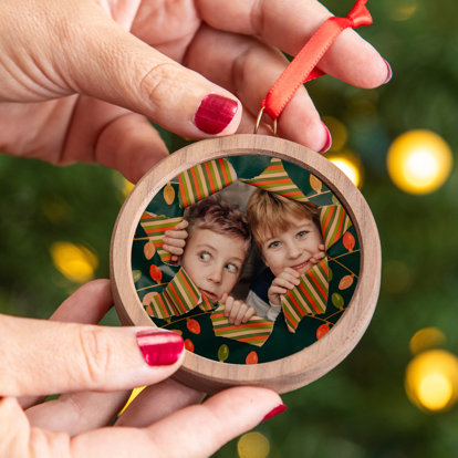 Hands holding a circle shaped framed ornament with a photo of two boys peaking out from behind a hole in a wrapping paper covered wall.
